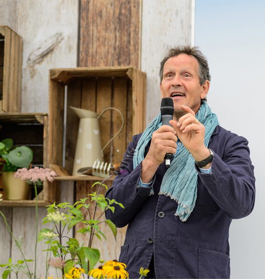 Monty Don speaking live onstage, with microphone in hand, at BBC Gardeners' World Live